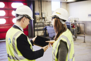 Man and woman wearing hi-vis and hard hats using Assure360 on iPad